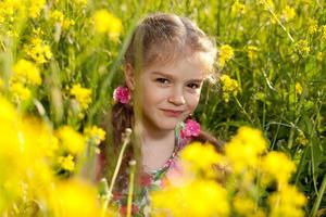 kleines Mädchen sitzt im Gras und Blumen foto