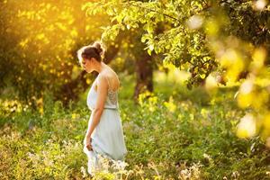 Frau in blauem Kleid geht in einem Apfelgarten spazieren foto
