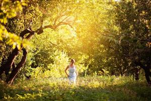 Mädchen im blauen Kleid geht durch den abendlichen Obstgarten foto