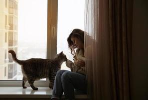 Mädchen sitzt am Fenster neben einer Katze foto
