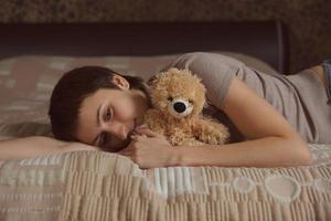 junge Frau liegt mit einem Teddybären auf dem Bett