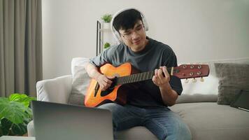 jung gut aussehend Mann spielen akustisch Gitarre Sitzung auf das Sofa im das Leben Zimmer beim heim. foto