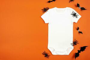 Halloween Weiß Baby Mädchen oder Junge Bodysuit Attrappe, Lehrmodell, Simulation eben legen mit Spinnen und Fledermäuse auf Orange Hintergrund. Design Strampler Vorlage, drucken Präsentation spotten hoch. oben Sicht. foto