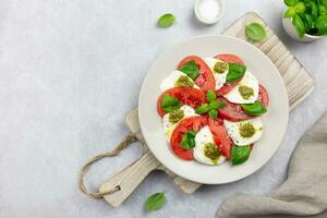 traditionell Italienisch Caprese Salat mit geschnitten Tomaten, Mozzarella, Basilikum, Pesto Soße und würzen auf ein Licht grau Beton Hintergrund. oben Sicht. Kopieren Raum. foto