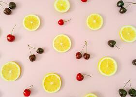 kreativ Obst Muster gemacht von rot Kirschen und Gelb Zitrone Scheiben auf Licht Pastell- Rosa Hintergrund. minimal Kirsche Obst und Zitrusfrüchte Layout. Natur Sommer- Muster Konzept. eben legen Sommer- Essen Idee. foto