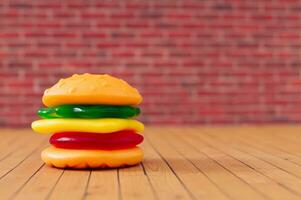 kreativ Layout von groß Burger gemacht von bunt gummiartig Süßigkeiten gegen rot Backstein Mauer Hintergrund. minimal Essen Konzept. lecker Gelee Süßigkeiten Komposition. gummiartig Süßigkeiten ästhetisch. foto