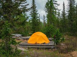 Orange Zelt Camping im das Taiga, ein Single Zelt auf ein hölzern Sockel im das Abend. Schlecht Wetter auf ein Wanderung, Camping im das Regen. Camping Leben Konzept. foto