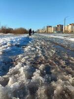 Frühling auftauen im das Stadt, ein schwierig Fußgänger Straße im das erweicht Schnee. Pfützen von geschmolzen Schnee auf das Straße. foto