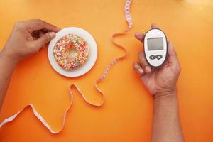 Hand halten diabetische Messwerkzeuge und Donuts auf Orange