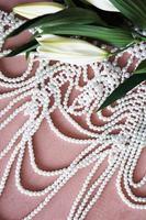 weiße Lilien und eine Perlenkette auf rosa Hintergrund.