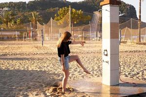 ein Mädchen in kurzen Hosen und einem schwarzen T-Shirt am Strand in der Nähe der Dusche. foto