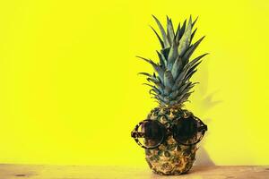 Ananas mit Sonnenbrille auf hölzern Tabelle und Gelb Mauer Hintergrund. foto