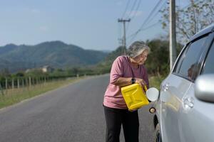 das Auto lief aus von Gas und ins Stocken geraten neben das Straße im Vororte und ein Alten asiatisch Frau benutzt ein Gallone von schonen Gas zu Treibstoff das Wagen. ein Frau bereitet vor ein Gallone von schonen Gas zu Treibstoff Vor reisen. foto