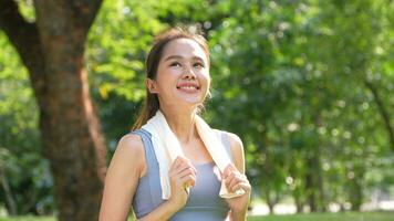 Porträt jung asiatisch Frau attraktiv lächelnd und verwenden Weiß Handtuch ruhen nach trainieren. lächelnd sportlich jung Frau Arbeiten aus draußen und suchen beim Kamera. gesund Lebensstil Gut Sein Wellness foto