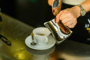 Hände von jung Frau Barista Gießen gedämpft cremig Milch auf Cappuccino Tasse beim das Bar Schalter. foto