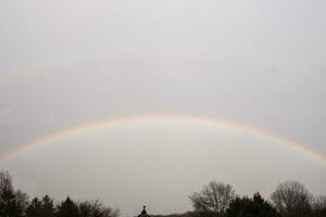 diese schön doppelt Regenbogen können Sein mit mit ein grau Himmel im das Hintergrund. das bunt Bogen ist gehen über das Bäume. foto