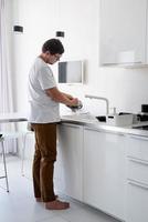 Mann im weißen T-Shirt beim Abwasch in der Küche foto