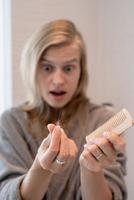 Frau, die sich die Haare bürstet, die an Haarausfall leidet foto