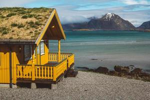 gelbes Holzhaus mit Moos auf dem Hintergrund des Meeres und der Berge foto