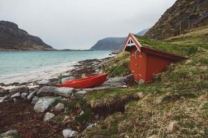 rotes Haus mit Moos auf dem Dach und Boot auf dem Hintergrund von Meer und Berg foto