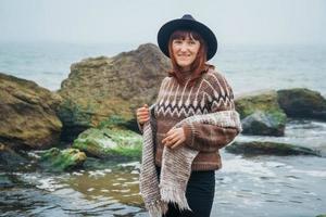 Porträt einer Frau mit Hut und Schal auf dem Hintergrund von Meer und Felsen foto
