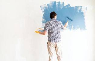 Mann färbt Wand blau mit einer Walze foto