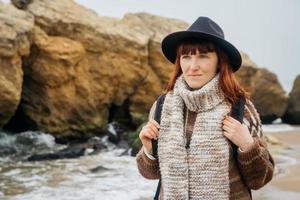 Frau mit Hut mit Rucksack auf dem Hintergrund von Meer und Felsen foto