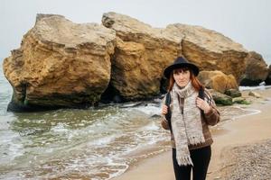 Frau mit Hut mit Rucksack auf dem Hintergrund von Meer und Felsen foto