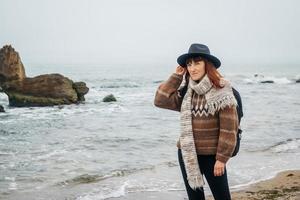 Frau mit Hut mit Rucksack auf dem Hintergrund von Meer und Felsen foto