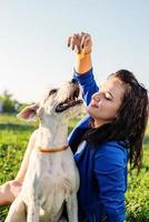 schöne junge frau, die im gras sitzt und ihren hund im park umarmt foto