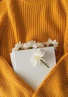 Draufsicht auf ein Buch mit weißen Chrysanthemenblüten auf gelbem Pullover foto
