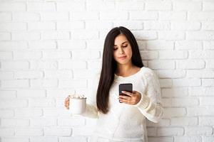 Frau mit einer Tasse Marshmallow-Kakao und ihrem Telefon foto