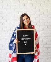 Frau mit amerikanischer Flagge, die Brieftafel mit den Worten glücklicher Unabhängigkeitstag hält und Friedenszeichen zeigt foto