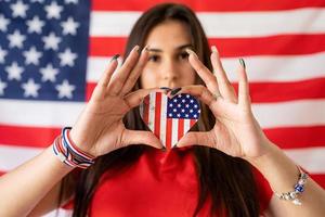 Frau, die eine herzförmige Nationalflagge auf dem Hintergrund der USA-Flagge hält foto
