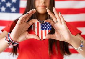 Frau, die eine kleine Nationalflagge auf dem Hintergrund der USA-Flagge hält foto