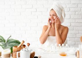 Frau im weißen Badetuch Auftragen von Gesichtscreme bei Spa-Behandlungen