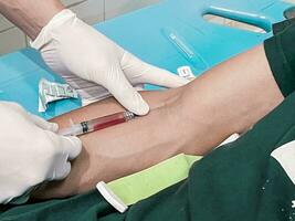 ein männlich Krankenschwester ist spritzen ein Schmerzen Reliever Betäubung in ein Patienten Hand foto