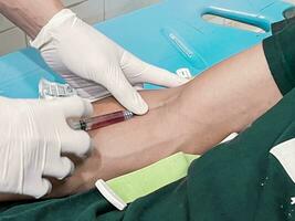 ein männlich Krankenschwester ist spritzen ein Schmerzen Reliever Betäubung in ein Patienten Hand foto