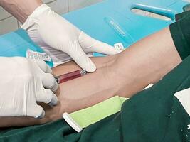 ein männlich Krankenschwester ist spritzen ein Schmerzen Reliever Betäubung in ein Patienten Hand foto