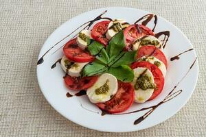 Weiß Teller von gesund klassisch köstlich Caprese Salat mit Tomaten und Mozzarella Käse mit Basilikum Blätter und Streifen von Soja Soße. Italienisch Konzept. foto