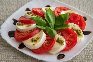 Teller von gesund klassisch köstlich Caprese Salat mit Tomaten und Mozzarella Käse mit frisch Basilikum Blätter auf Licht Leinen- Tischdecke. Italienisch Küche Konzept foto