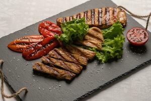 gegrillt Truthahn Brust geschnitten Steaks mit gebacken Pfeffer, Grüner Salat und Tomate auf ein schwarz Tafel. horizontal Orientierung, Nahansicht foto