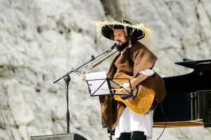 ein Mann im ein Hut und ein lange Mantel spielen ein Gitarre foto