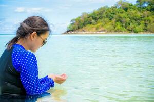 asiatisch Frau aussehen beim das klar Wasser im ihr Hände auf das Meer foto