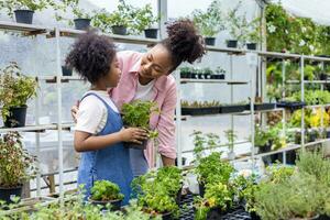 afrikanische mutter und tochter wählen gemüse- und kräuterpflanzen aus der örtlichen gärtnerei mit einkaufswagen voller sommerpflanzen für wochenendgärtnern und im freien foto