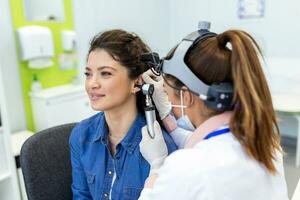 Hören Prüfung. HNO-Arzt Arzt Überprüfung Frau Ohr mit Otoskop oder Auriskop beim medizinisch Klinik. Hals-Nasen-Ohrenarzt ziehen Ohr mit Hand und suchen beim es mit Otoskop Nahaufnahme. foto