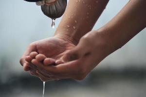 Hand fängt Wassertropfen auf, die aus dem Wasserhahn kommen foto