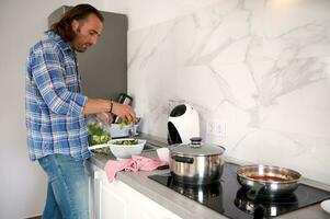 Seite Porträt von gut aussehend kaukasisch Mann vorbereiten Abendessen im das Zuhause Küche foto