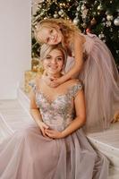 Tochter umarmt ihre Mutter, während sie am Weihnachtsbaum sitzt foto