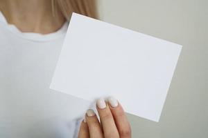 Frau im weißen T-Shirt hält weißes leeres Papierblatt in der Hand foto